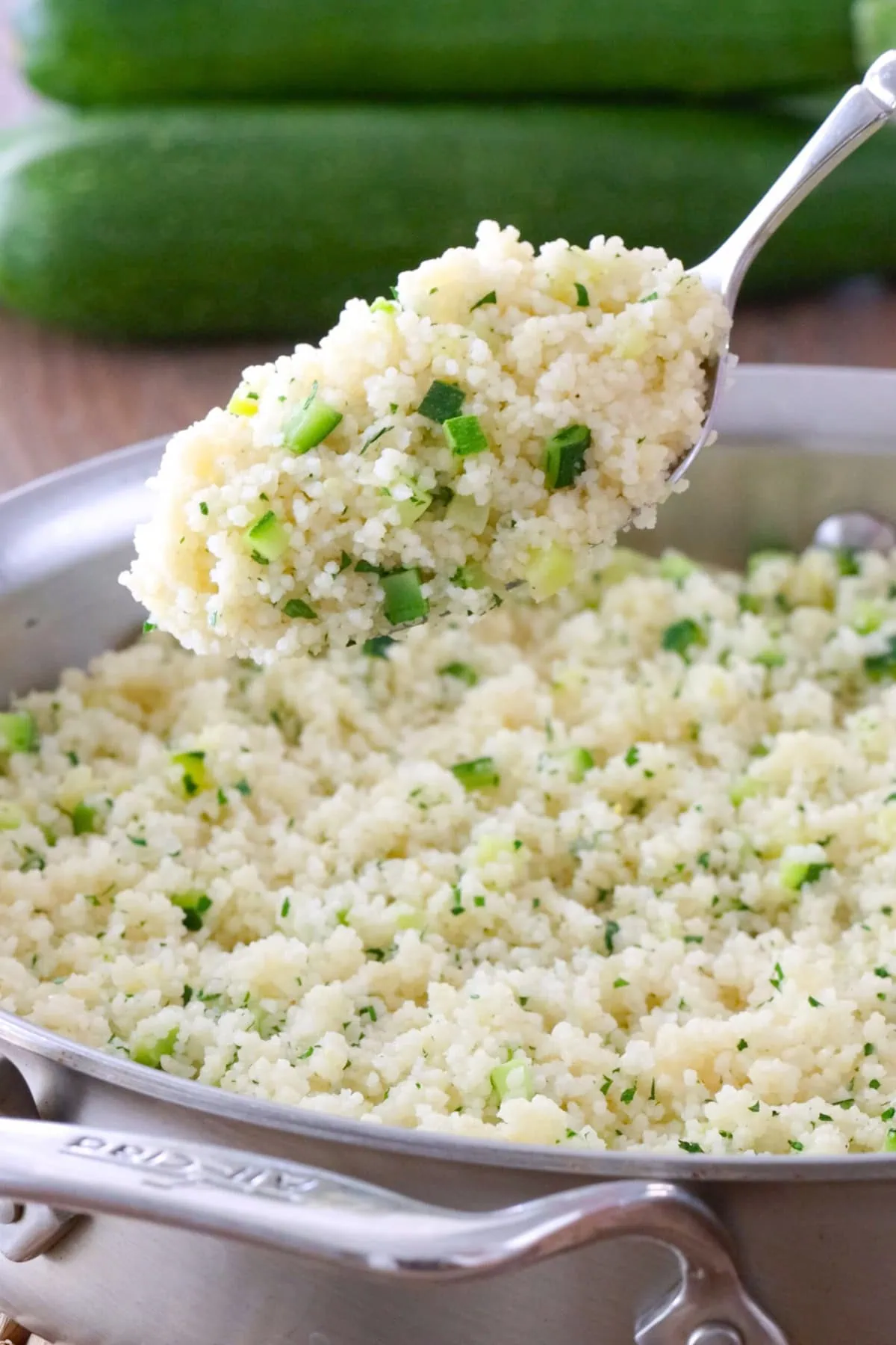 A spoonful of zucchini couscous held over a skillet holding more couscous.