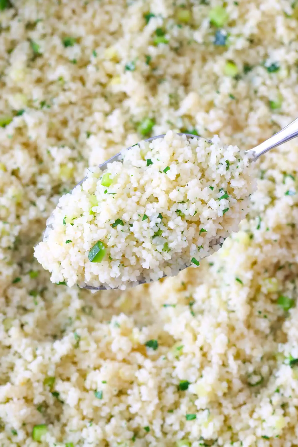 Close up shot of Zucchini Couscous on a large spoon, with more couscous in the background. 