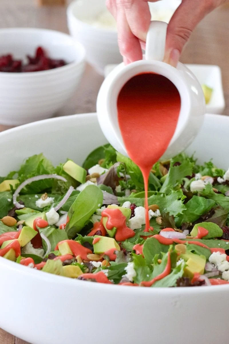 Raspberry Vinaigrette Salad made with a homemade vinaigrette , lettuce greens, pepitas, feta cheese, avocados and dried cranberries. 