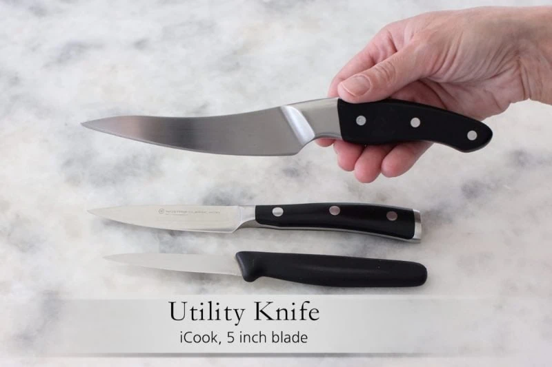 Best kitchen knives - utility knife held up over several paring knives. 