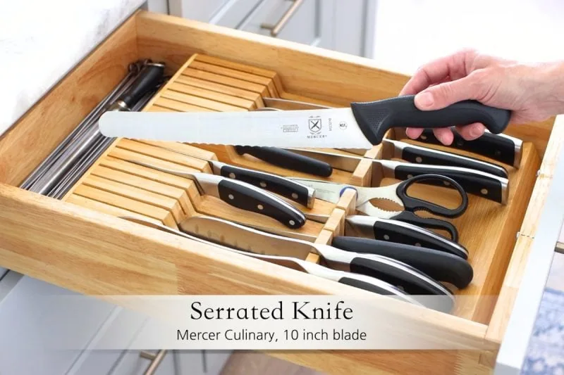 Best kitchen knives - serrated knife, bread knife held over a kitchen drawer with knives in an organizer. 