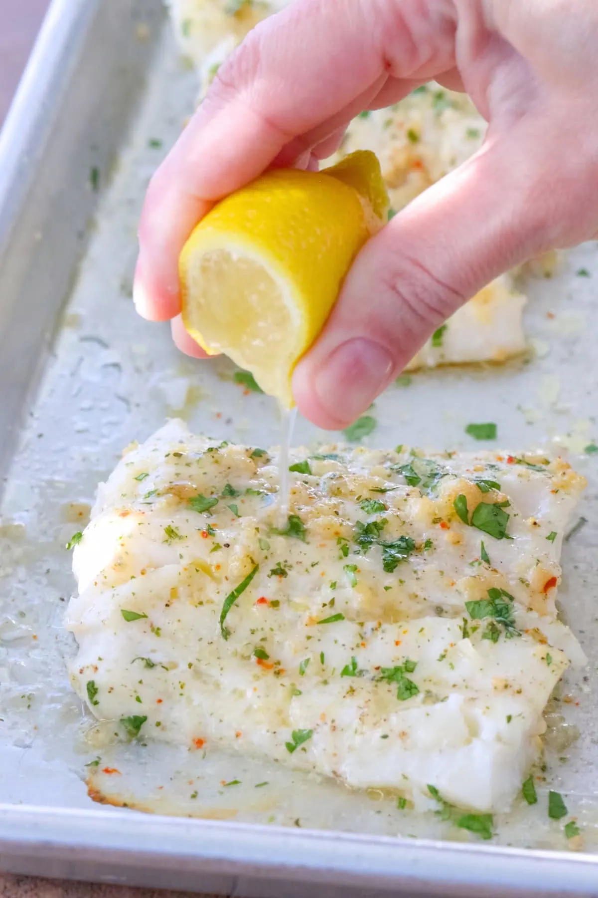 Baked cod on a sheet pan with lemon juice squeezed over it.