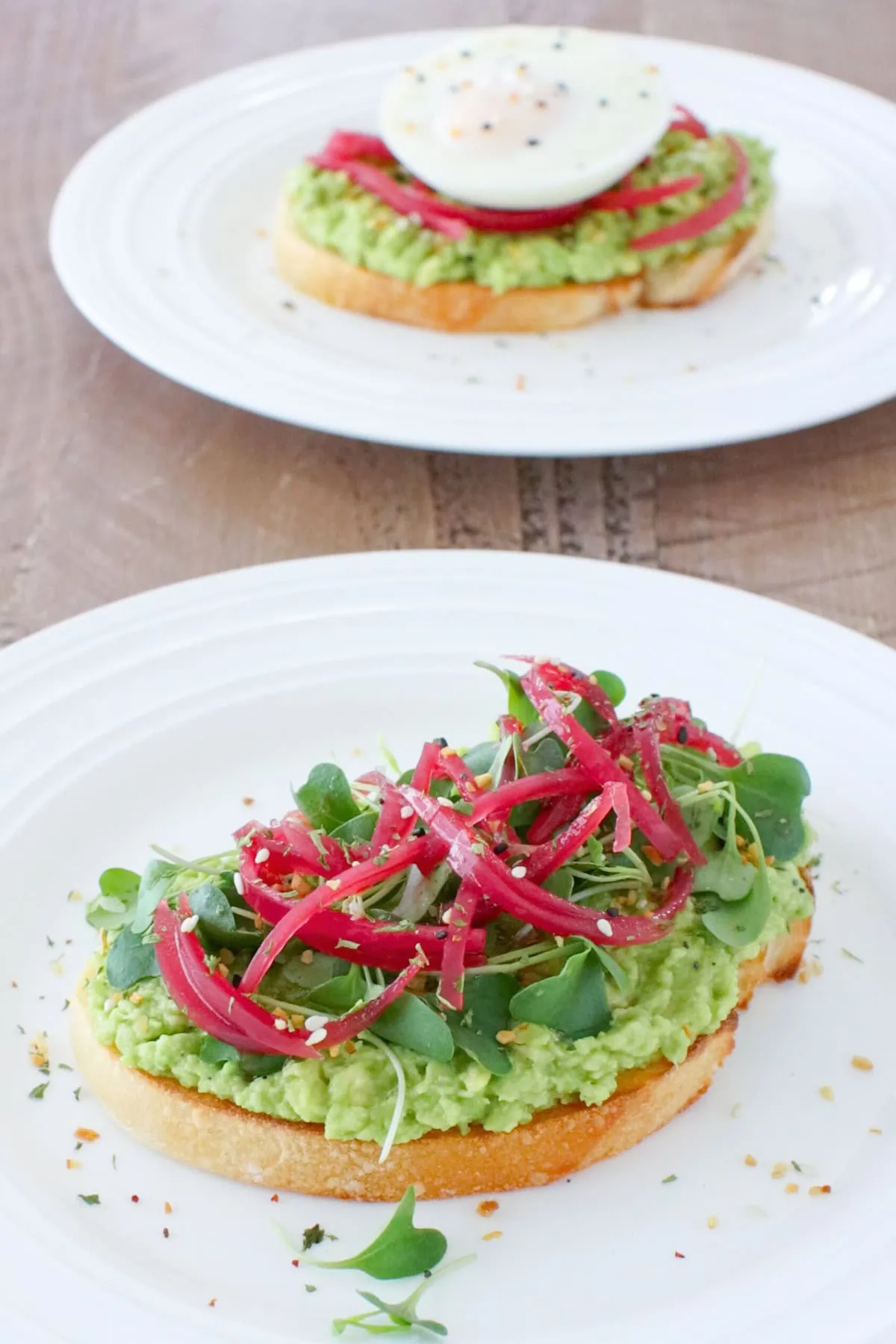 Avocado toast with pickled red onions and microgreens on a plate. 